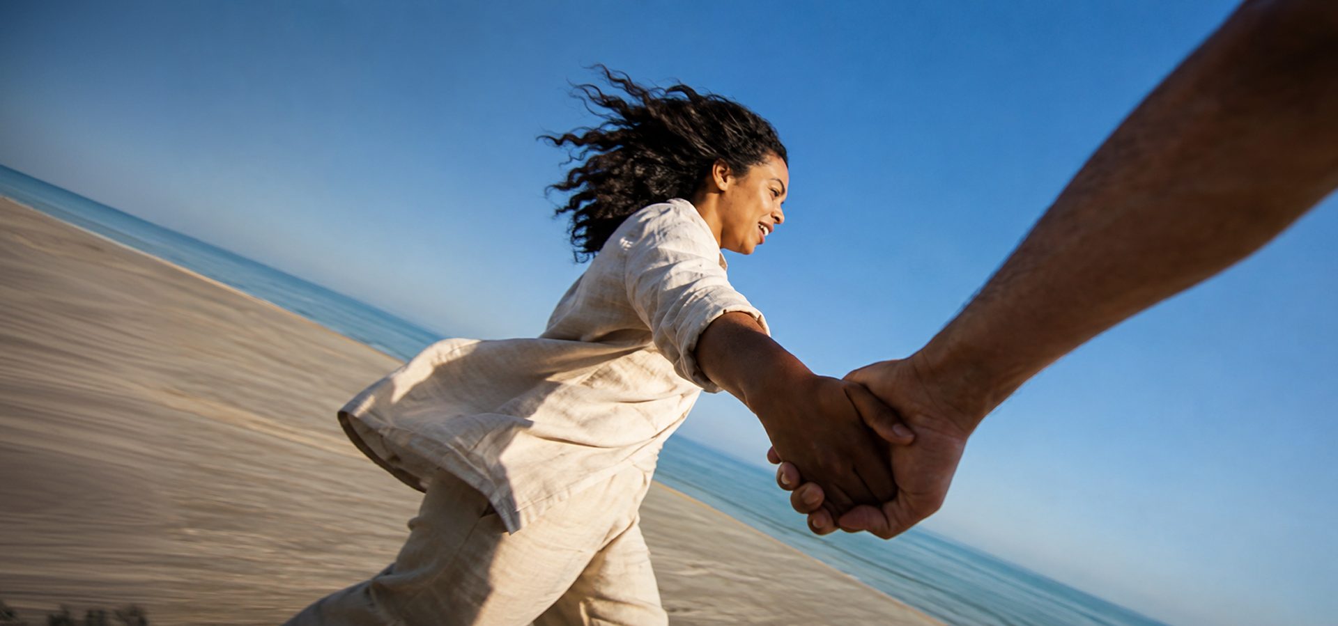 A woman running on a beach while holding someone's hand