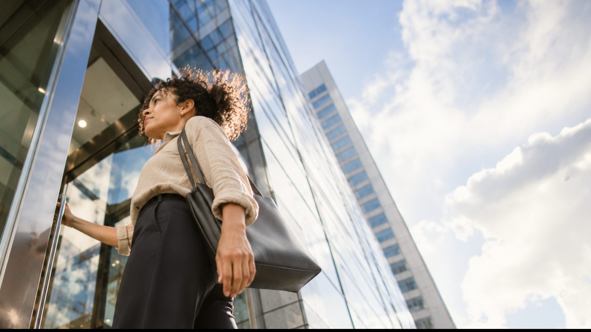 A woman with a shoulder bag walking past a glass office building