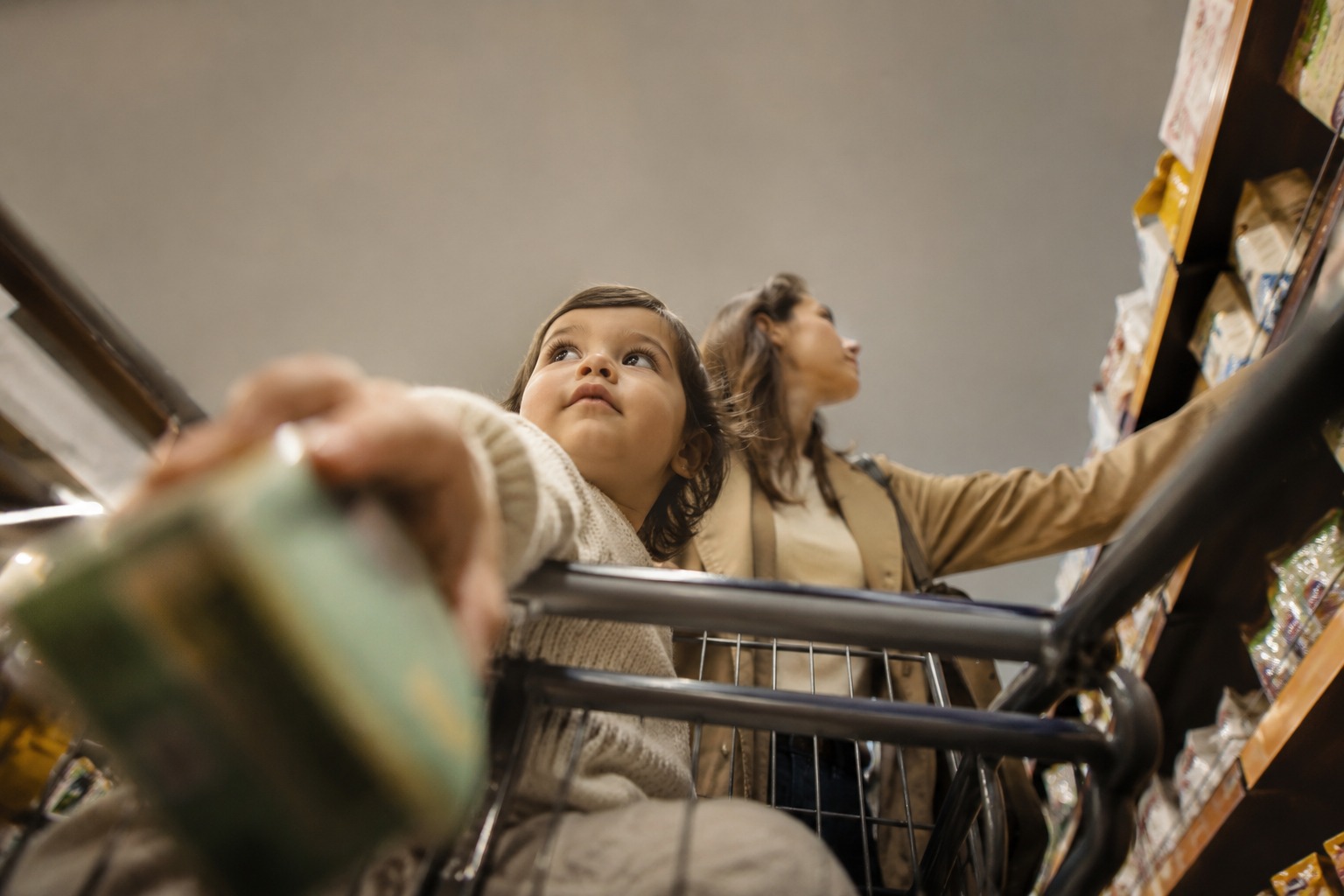 A mother and young child reaching for groceries in a supermarket aisle