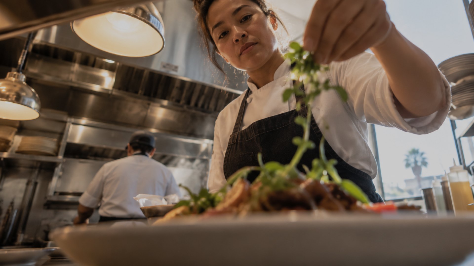 A chef finishing a dish with fresh herbs in a restaurant kitchen
