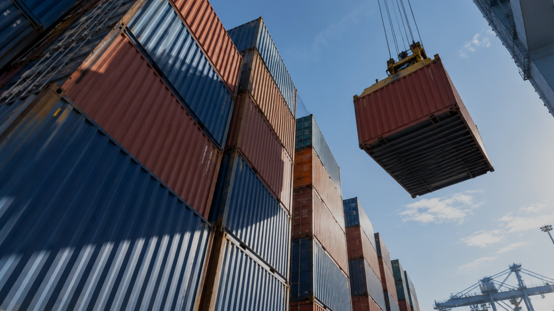 Shipping containers stacked at a port, one lifted by a crane