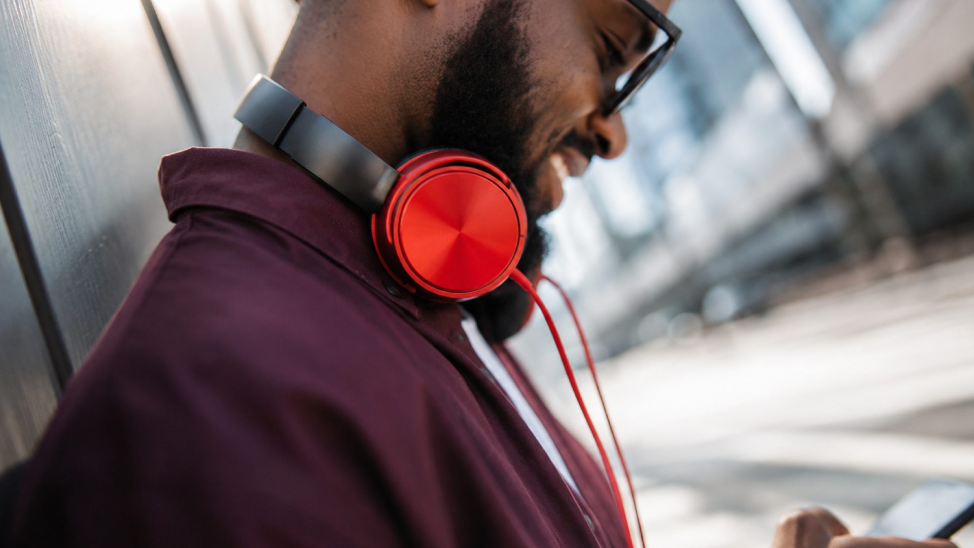 A man wearing red headphones and glasses looking down at his phone