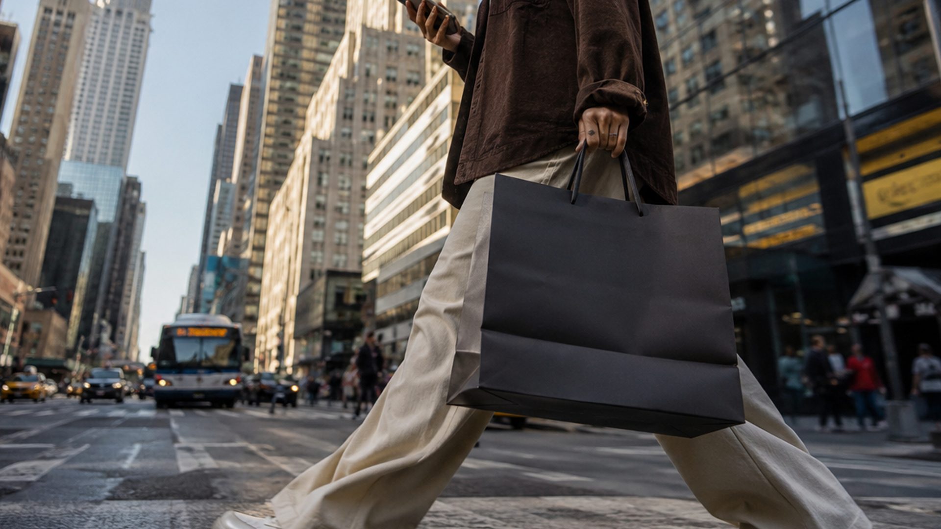 A woman crossing a city street carrying a dark shopping bag